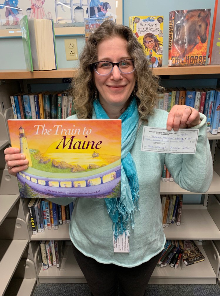 Youth librarian Rachel Davis with a Rotary Club check supporting Thomas Memorial Library's youth literacy programs and a book donated through the Rotary by The Downeaster train.