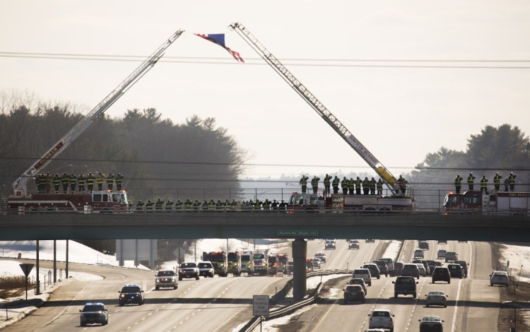 Firefighters line up Sunday afternoon on the Buxton Road bridge over the Maine Turnpike in Saco as a procession carrying the body of Berwick Fire Capt. Joel Barnes heads to the Old Orchard Beach Funeral Home, where a private family ceremony is expected to be held this week. Barnes died while battling an apartment building fire in Berwick on Friday.