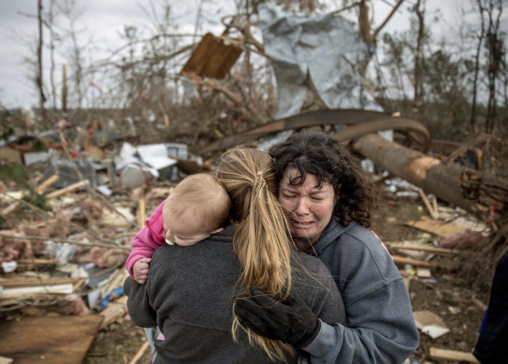 Carol Dean, right, cries while embraced by Megan Anderson and her 18-month-old daughter Madilyn at her destroyed home in Beauregard, Ala.