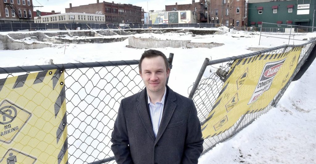 Brian Clark, vice president of planning at Colby College, stands Thursday beside the fenced-in area of the former Camden National Bank and former Levine's building in downtown Waterville that will become the site of a hotel complex.