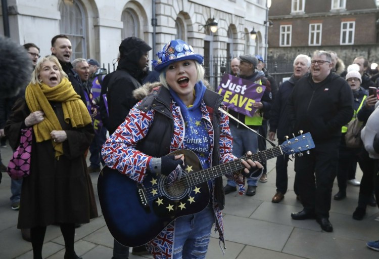 An anti-Brexit supporter of remaining in the European Union, center, plays a guitar as she's surrounded by pro-Brexit supporters outside the Houses of Parliament in London on Thursday.