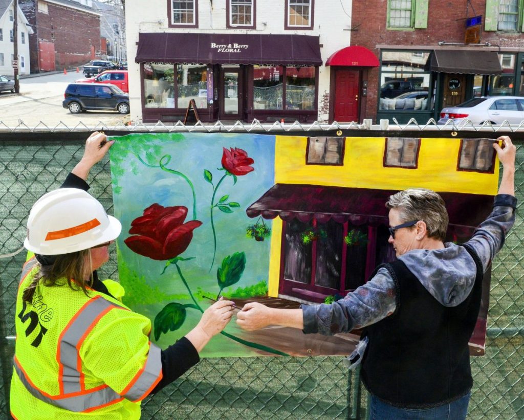 Kennebec Journal file photo by Joe Phelan 
 Karen Libby, the Maine Department of Transportation resident for the Water Street project, left, and Deb Fahy, executive director of the Harlow Gallery, hang a mural in April 2018 on the sidewalk side of the construction fence on on Water Street in downtown Hallowell.