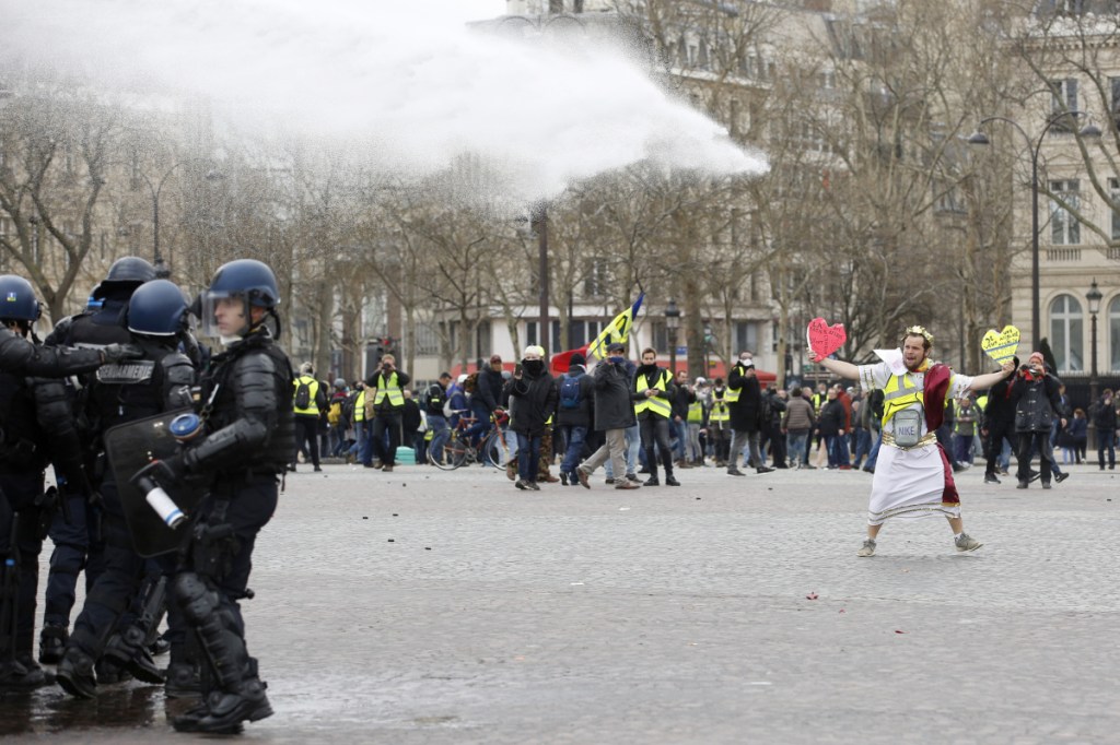 A demonstrator faces police water cannons in Paris. French yellow vest protesters clashed Saturday with riot police near the Arc de Triomphe as they kicked off their 18th straight weekend of demonstrations against President Emmanuel Macron. (AP Photo/Christophe Ena)