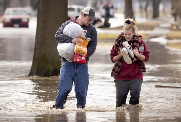 Anthony Thomson, left, and Melody Walton make their way out of a flooded neighborhood Sunday in Fremont, Neb.