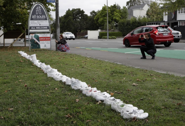 In front of a church Tuesday in Christchurch, New Zealand, people photograph a memorial of 50 pairs of white shoes for the victims of the massacre at two mosques Friday. Four days after the attack, New Zealand's deadliest shooting in modern history, relatives were anxiously waiting for word on when they can bury their loved ones.