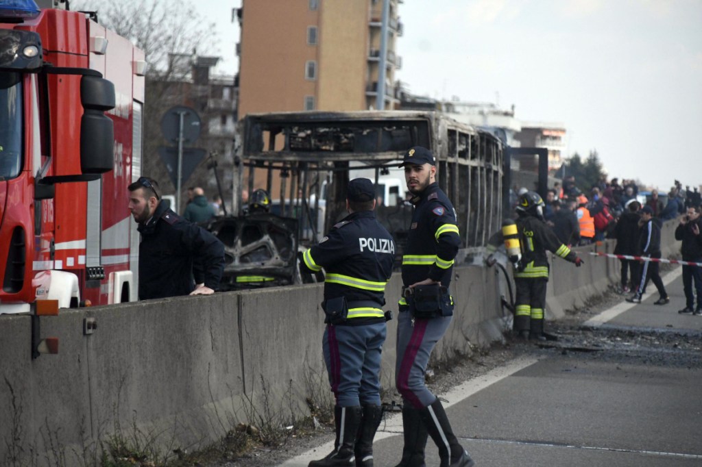 Firefighters and police officers stand guard over a school bus in San Donato Milanese, Italy, on Wednesday after the driver kidnapped 51 children and their chaperones and threatened to kill them.