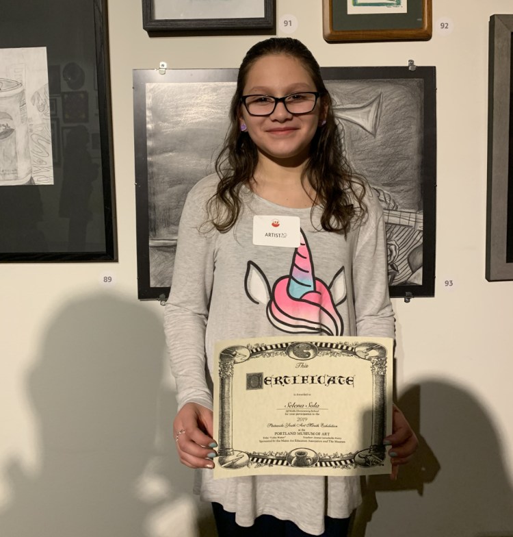 Wells fourth-grader Selena Sola poses next to her artwork on display at the Portland Museum of Art. She is one of three Wells-Ogunquit Community School District students selected to display their art.