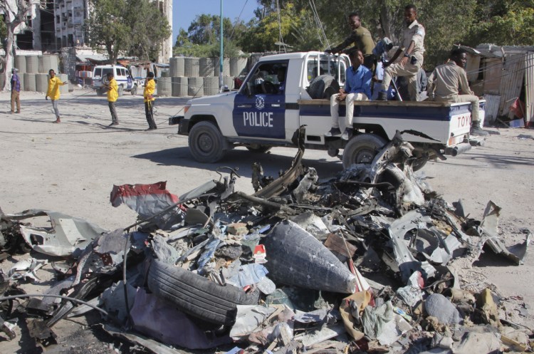 A police vehicle drives past wreckage Saturday after a suicide car bombing outside a government building in Mogadishu, Somalia. Gunmen stormed the building, killing at least five people, including the country's deputy labor minister, police said. 