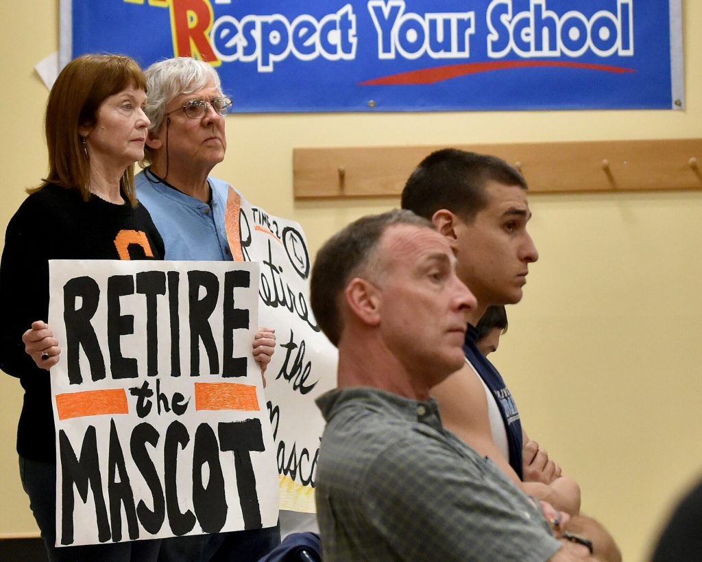 Linda Savage, back left, and Mark Roman, back center, stand with signs calling for the Skowhegan Area High School Indian mascot be retired during an April 7, 2016, School Administrative District 54 board meeting at Skowhegan Area Middle School. 