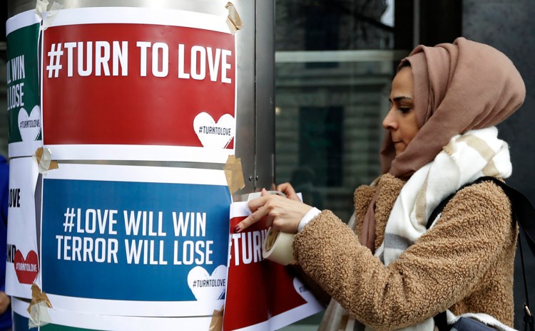 A demonstrator hangs banners from multi-faith group 'Turn to Love' during a vigil at New Zealand House in London, Friday, March 15, 2019. Multiple people were killed in mass shootings at two mosques full of worshippers attending Friday prayers on what the prime minister called "one of New Zealand's darkest days," as authorities detained four people and defused explosive devices in what appeared to be a carefully planned attack. 
