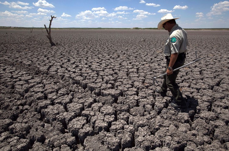 In this Aug 3, 2011 file photo, Texas State Park police officer Thomas Bigham walks across the cracked lake bed of O.C. Fisher Lake, in San Angelo, Texas. The impacts of record-breaking heat and years of low or no rainfall can be felt years after a dry spell passes. 