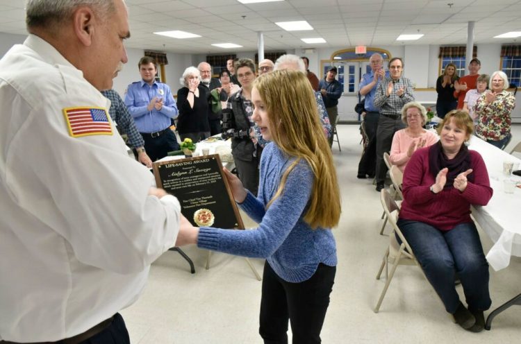 China Village Fire Chief Tim Theriault presents a plaque to Aislynn Savage, 12, Tuesday during the annual Fire Department meeting in China. Aislynn's mother, Laura, right, and firefighters and family applaud. Aislynn was recognized for her actions on Feb. 23 when her mother had a medical incident while driving. Aislynn took the wheel and guided the car safely into a snowbank. 