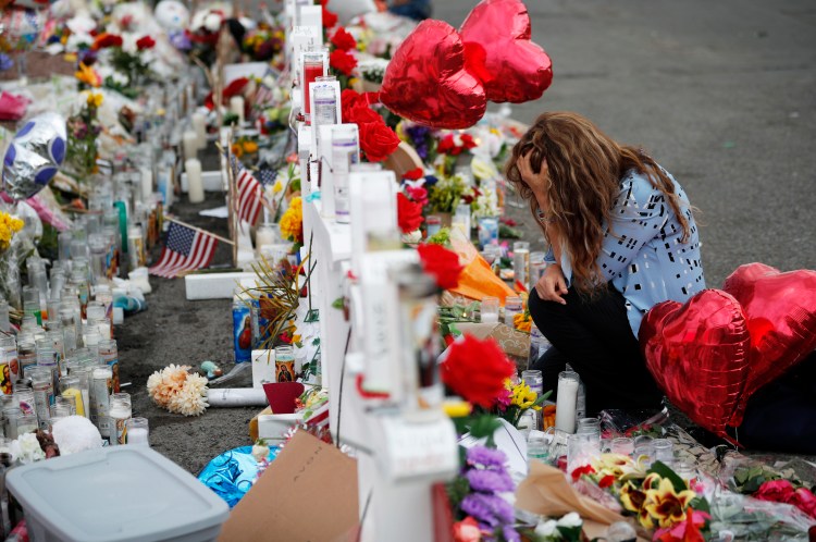 Gloria Garces kneels in front of crosses at a makeshift memorial near the scene of a mass shooting at a shopping complex Tuesday in El Paso, Texas. The border city jolted by a weekend massacre prepared for a visit from President Trump amid anger from El Paso residents and local Democratic leaders who say he isn't welcome and should stay away.  