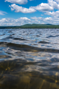 Photo taken close to the surface of the luscious water of Sebago Lake, looking west toward the mountains on a sunny day.