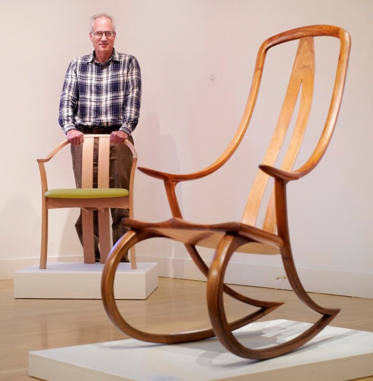Peter Korn, executive director of the Center for Furniture Craftmanship in Rockport, is retiring at the end of the year. Korn stands with one of his chair creations, Continuous-arm Chair, made of ash and leather. In the foreground is Monogram Rocking Chair by David Haig, made of walnut. 