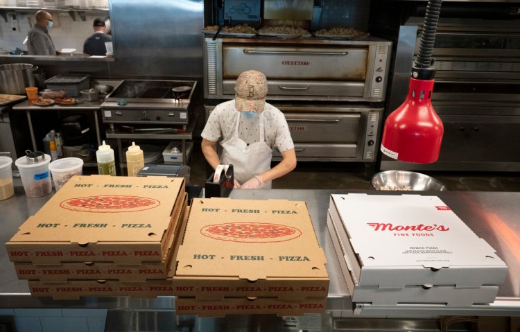 Patrick Pakulski, a line cook at Monte’s Fine Foods in Portland, works the line behind empty pizza boxes constructed in advance of the Friday night rush. Because of supply chain disruptions, Monte's hasn't been able to get the usual branded pizza boxes it uses, seen at right, and has to use generic ones. It has only a few branded boxes left.