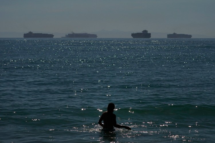 A man wades through the water in Seal Beach, Calif., on Oct. 1, as container ships waiting to dock at the Ports of Los Angeles and Long Beach are seen in the distance. The White House announced last week that the Los Angeles port will stay open 24 hours a day, seven days a week to clear the backlog.