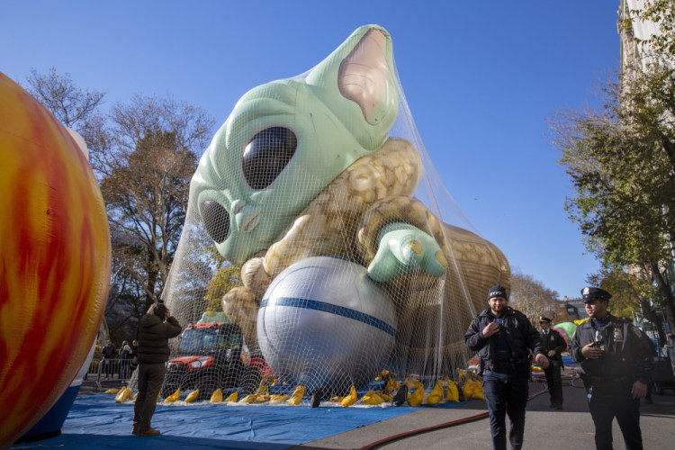 Police walk by an inflated helium balloon of Grogu, also known as Baby Yoda, from the Star Wars show The Mandalorian, Wednesday in New York, as the balloon is readied for the Macy's Thanksgiving Day Parade on Thursday. 