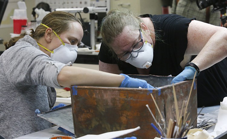 Sue Donovan, left, and Kate Ridgeway dig into the artifacts inside a copper box time capsule recovered from the base of a Robert E. Lee monument, on Tuesday at the Virginia Department of Historical Resources lab in Richmond, Va. 