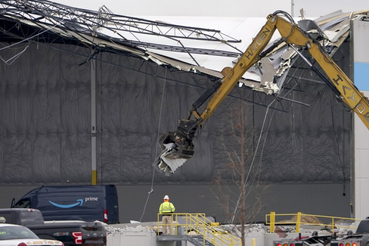 Workers use equipment to remove a section of roof left on a heavily damaged Amazon fulfillment center Saturday, Dec. 11, 2021, in Edwardsville, Ill. The a large section of the roof of the building was ripped off and walls collapsed when a strong storms moved through area Friday night. 