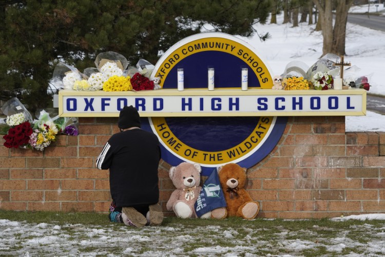 A visitor kneels to pray at a memorial on the sign of Oxford High School in Oxford, Mich., on Wednesday. A 15-year-old sophomore opened fire at the school, killing several students and wounding multiple other people, including a teacher. 