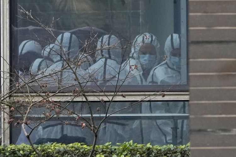 Members of a World Health Organization team are seen through a window during a field visit to the Hubei Animal Disease Control and Prevention Center in Wuhan in central China's Hubei province on Feb. 2. Nearly two years into the COVID-19 pandemic, the origin of the virus tormenting the world remains shrouded in mystery. 
