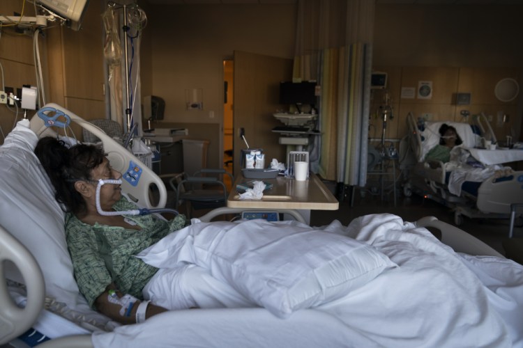 Natalie Balli, 71, and her twin sister, Linda Calderon, background right, watch TV as they rest in their beds in a COVID-19 unit at Providence Holy Cross Medical Center in Los Angeles on Friday. They were admitted to the hospital on the same day, a few days after their Thanksgiving gathering. “We really regret not getting the shots because if we did, we wouldn’t be like this right now,” Calderon said.
