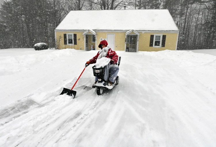 Dee Robbins, 70, guides her snow shovel while driving her motorized scooter down her home’s driveway Monday during a snowstorm in Waterville. Robbins made several shoveling passes before going back inside her home to warm up and charge the scooter's battery. Snow fell inland, but along the coast the storm brought mostly rain and high wind.