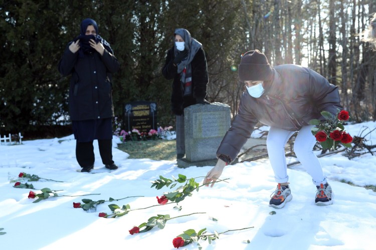 Hawa Zaman places roses on the unmarked grave of her grandfather, Mohammad Safai, in Evergreen Cemetery, while her grandmother, Shafia Safai, left, and mother, Marzia Zaman, look on.