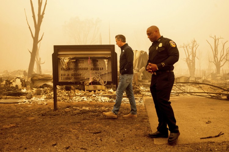 California Gov. Gavin Newsom examines a church marquee while visiting Greenville, which suffered extensive structure loss during the Dixie Fire, on Aug. 7, 2021, in Plumas County, Calif. Accompanying him is Cal Fire Assistant Region Chief Curtis Brown. Democratic governors such as California's Newsom and Washington's Jay Inslee have been clear about their plans to boost spending on climate-related projects, including expanding access to electric vehicles and creating more storage for clean energies such as solar. 