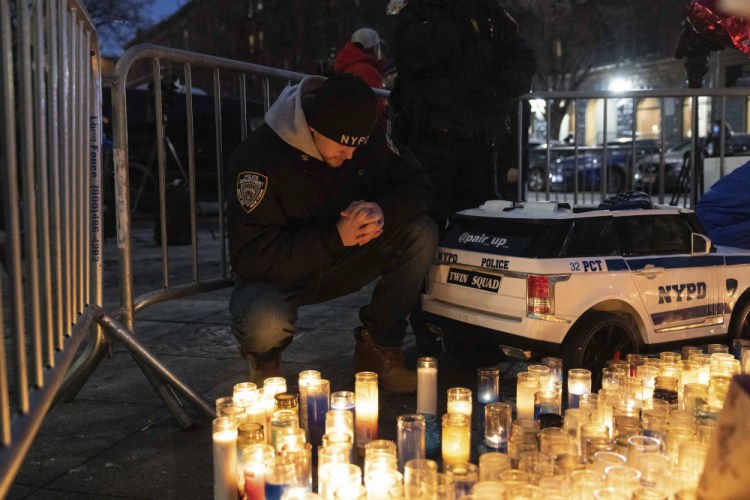 A police officer prays at a makeshift memorial Monday outside the New York City Police Department's 32nd Precinct, near the scene of a shooting days earlier in the Harlem neighborhood of New York. 