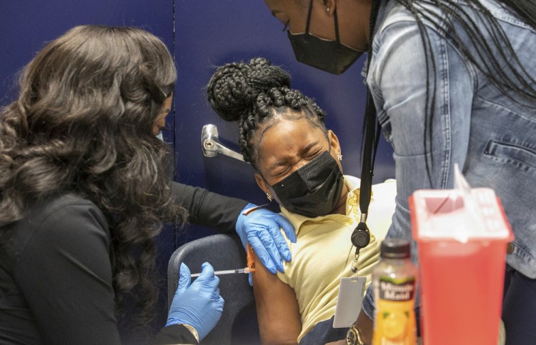 Medical assistant Micah Dubose, left, and Sandra Castro vaccinate squirming third-grader Hailey McDonald, 8, at KIPP Believe charter school in New Orleans on Jan. 25.

