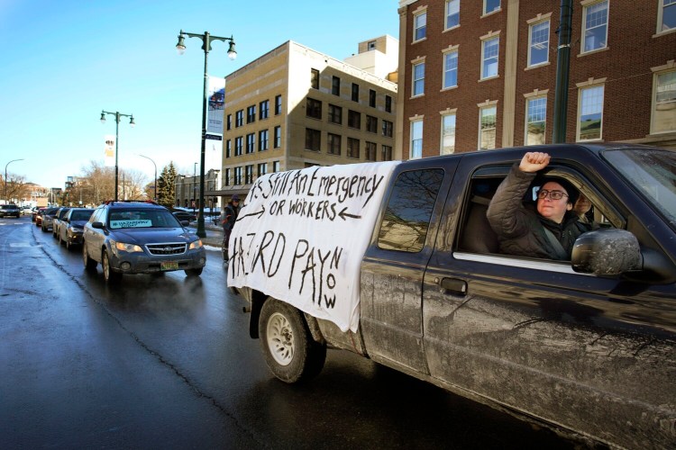 Drew Christopher Joy holds a fist out the window of a truck in solidarity while passing a rally at Portland City Hall  advocating for hazard pay. Joy is with the Southern Maine Workers' Center, which organized the rally, and was part of a convoy of vehicles that traveled from the Eastern Prom to City Hall. 