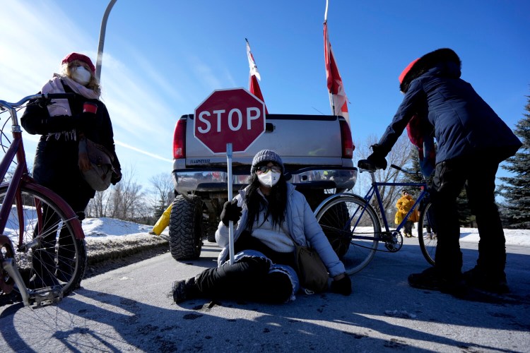 A counter protester holds a stop sign as they sit on the pavement behind a vehicle during a counter protest, preventing vehicles from driving in a convoy en route to Parliament Hill, on the 17th day of a protest against COVID-19 measures that has grown into a broader anti-government protest, in Ottawa, on Sunday. 