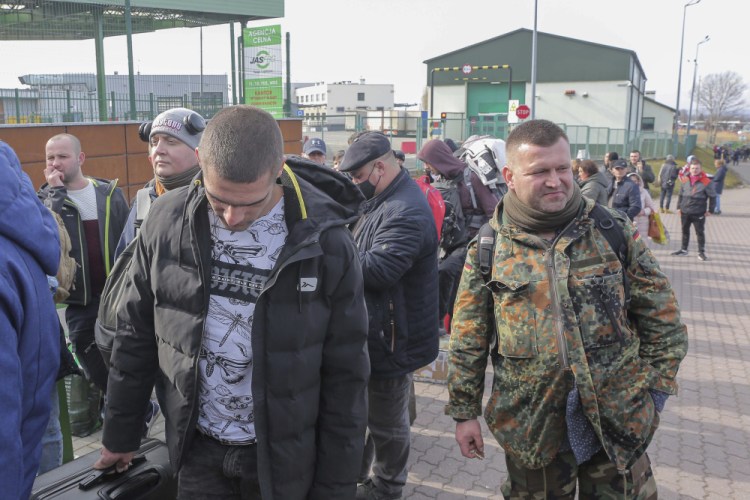 Polish volunteer Jedrzej, 34, in military uniform joins Ukranians, left, waiting to cross the border to go and fight against Russian forces, at Medyka border crossing Saturday in Poland.