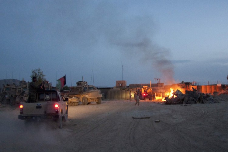 An Afghan National Army pickup truck passes parked U.S. armored military vehicles, as smoke rises from a fire in a trash burn pit in April 2011 at Forward Operating Base south of Kabul, Afghanistan.