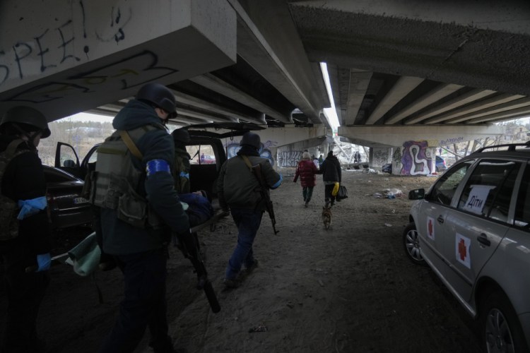 Ukrainians soldiers pass under a destroyed bridge as they evacuate an elderly resident in Irpin, northwest of Kyiv, Saturday, March 12, 2022. Kyiv northwest suburbs such as Irpin and Bucha have been enduring Russian shellfire and bombardments for over a week prompting residents to leave their homes. (AP Photo/Efrem Lukatsky)
