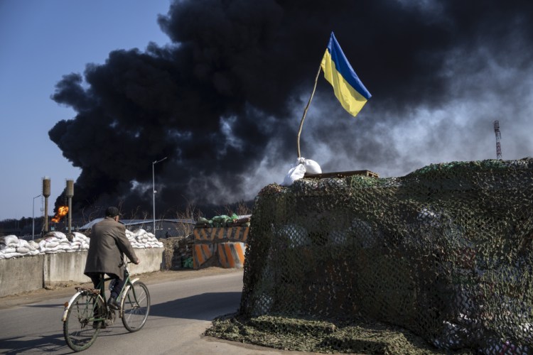 A man rides a bicycle as black smoke rises from a fuel storage of the Ukrainian army following a Russian attack, on the outskirts of Kyiv, Ukraine on Friday. 