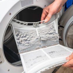 Hands are removing a dryer lint trap full of dust and dirt.