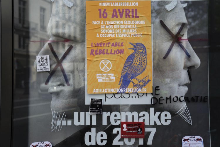 A torn front page ad shows incubent President Emmanuel Macron and challenger Marine Le Pen as the environmental group Extinction Rebellion takes part in a three-day demonstration Monday against what they call France's inaction on climate issues, in the district of Porte de Saint Denis in the center of Paris, France.