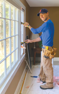 A man looks at the camera as he uses a hand tool to install a window.