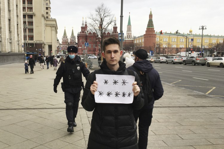 Police officers, left, prepare to detain Dmitry Reznikov holding a blank piece of paper with eight asterisks that could have been interpreted as standing for "No to war" in Russian, with the Kremlin in the background in Moscow, Russia, on March 13.