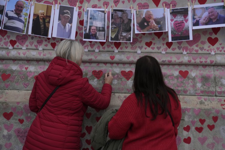 Family members write a message to two sisters who died of COVID on the National Covid Memorial wall in London on Tuesday.