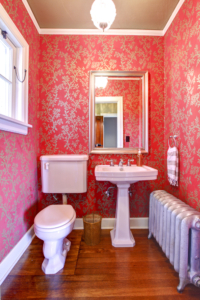 A vintage bathroom with steam radiator is decorated with red and gold wallpaper.