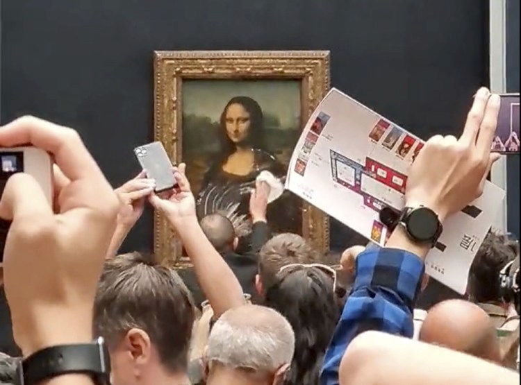 A security guard cleans the smeared cream from the glass protecting the Mona Lisa at the Louvre Museum, in Paris, France, on Sunday, after a man disguised as an old woman in a wheelchair threw a piece of cake at the glass protecting the painting. (@Klevisl007 via AP)
