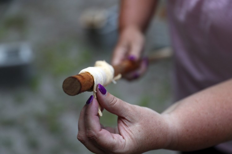  Elaine Taylor, of the Girl Scouts of Maine, wraps crescent roll dough around a wooden dowel to cook a dough boy over a campfire. 