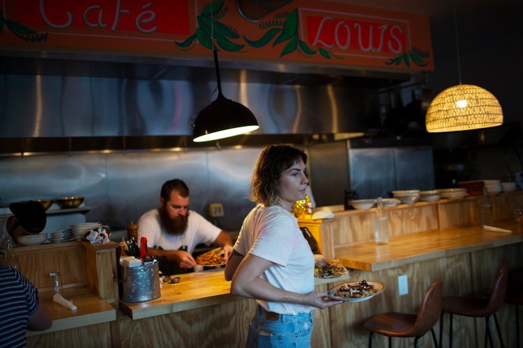 Bar manager Bryna Askins serves diners at Cafe Louis in South Portland, while chef and owner Evan Richardson (background) plates dishes in the open kitchen. 