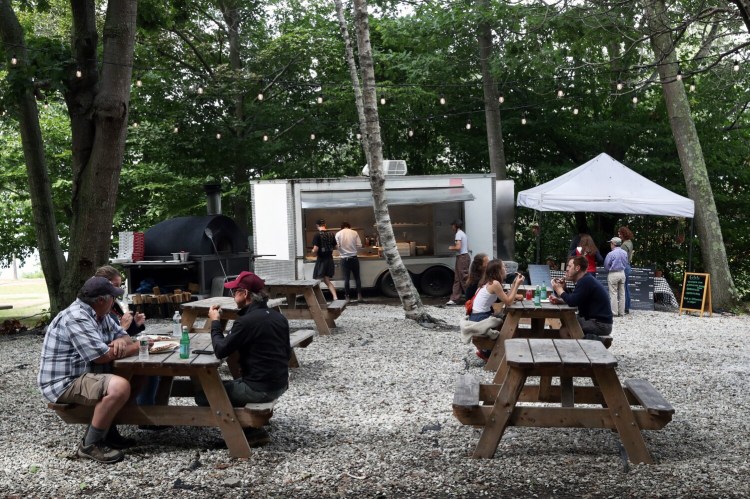 At the seasonal Il Leone, customers sit at picnic tables sit under a grove of trees near the water on Peaks Island. The pizza oven is in the background at left. 