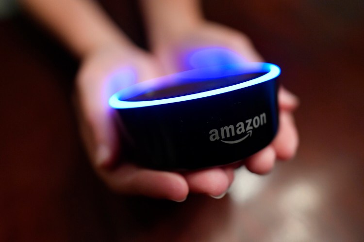 FILE - In this Aug. 16, 2018, file photo a child holds his Amazon Echo Dot in Kennesaw, Ga. From what you buy online, to how you remember tasks, to when you monitor your doorstep, Amazon is seemingly everywhere. And it appears the company doesn’t want to halt its reach anytime soon. In recent weeks, Amazon has said it will spend billions of dollars in two gigantic acquisitions that, if approved, will broaden its ever growing presence in the lives of consumers.    (AP Photo/Mike Stewart, File)