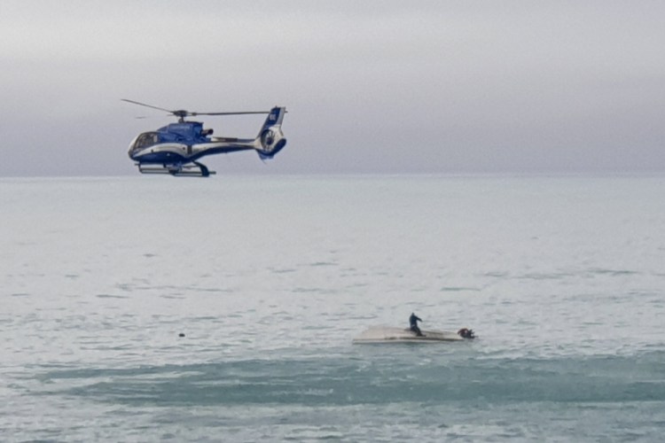 A helicopter flies overs an upturned boat with a survivor sitting on the hull off the coast of Kaikoura, New Zealand, on Saturday. A boat in New Zealand collided with a whale and capsized. 